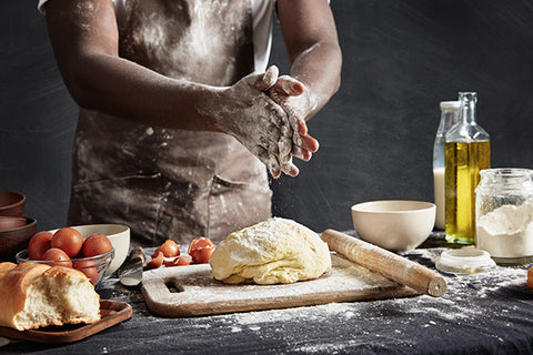 Person kneading dough with a rustic kitchen setting, including a loaf of bread and various ingredients.