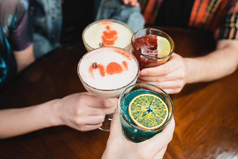 Four people holding colorful cocktails with a focus on their hands and drinks.