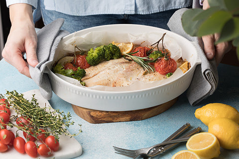 Dish of roasted chicken with vegetables on a table with lemons and herbs.