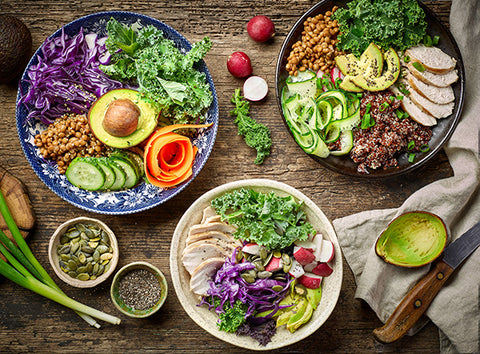 Plates of healthy food including salad, beans, and avocado on a wooden table.